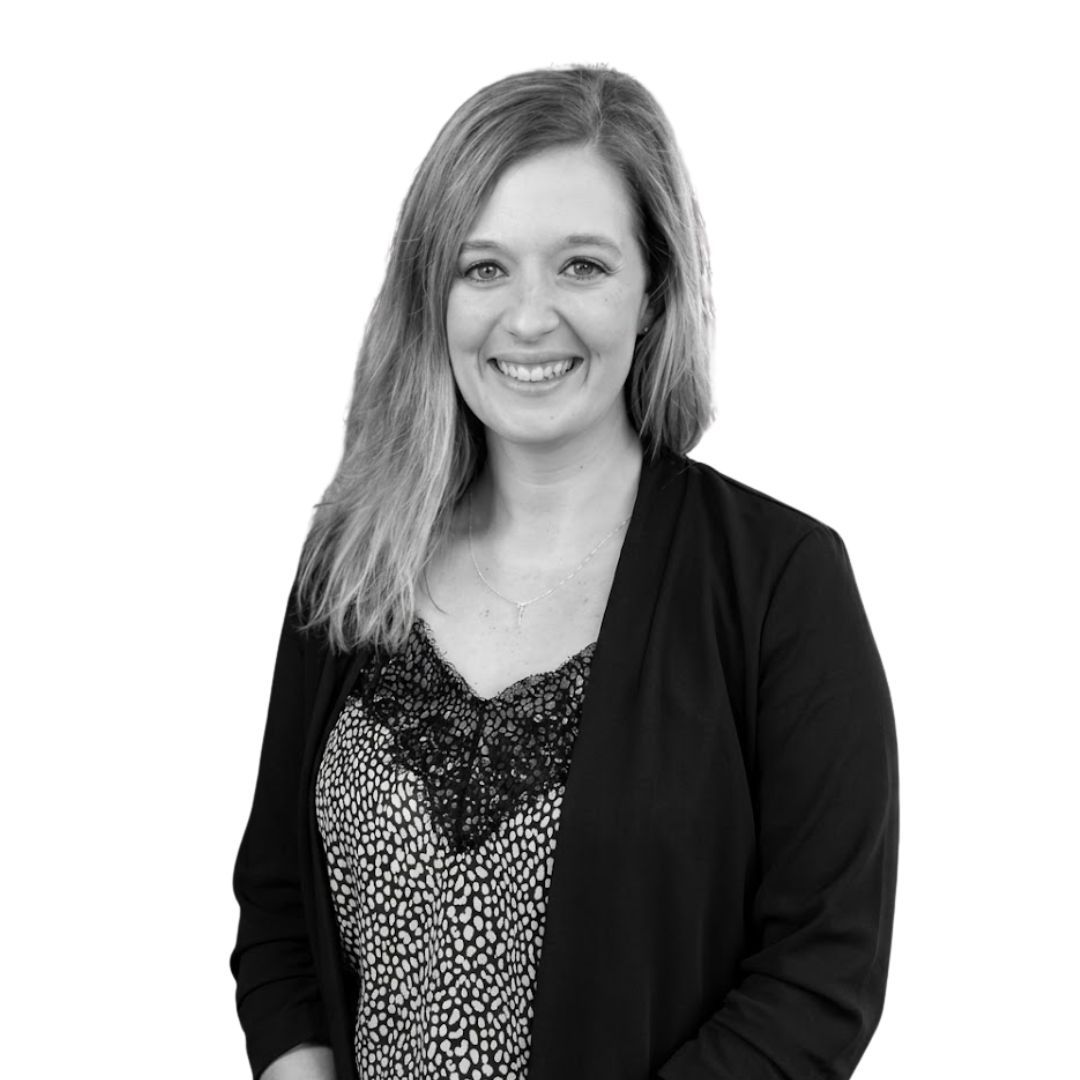Smiling woman with long straight hair wearing a patterned blouse and black blazer, facing forward against a plain background