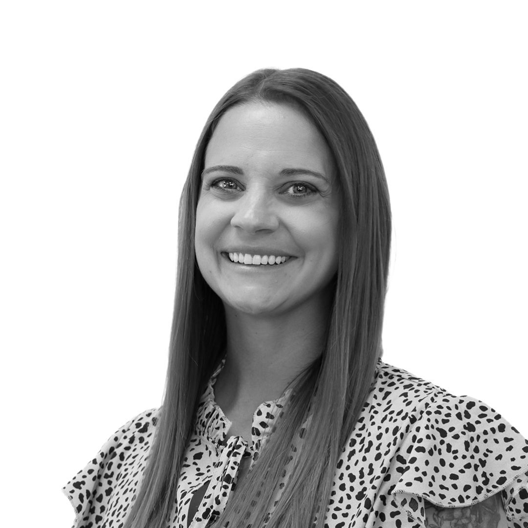 Smiling woman with long straight hair wearing a patterned blouse with ruffled sleeves, facing slightly to the side against a plain background