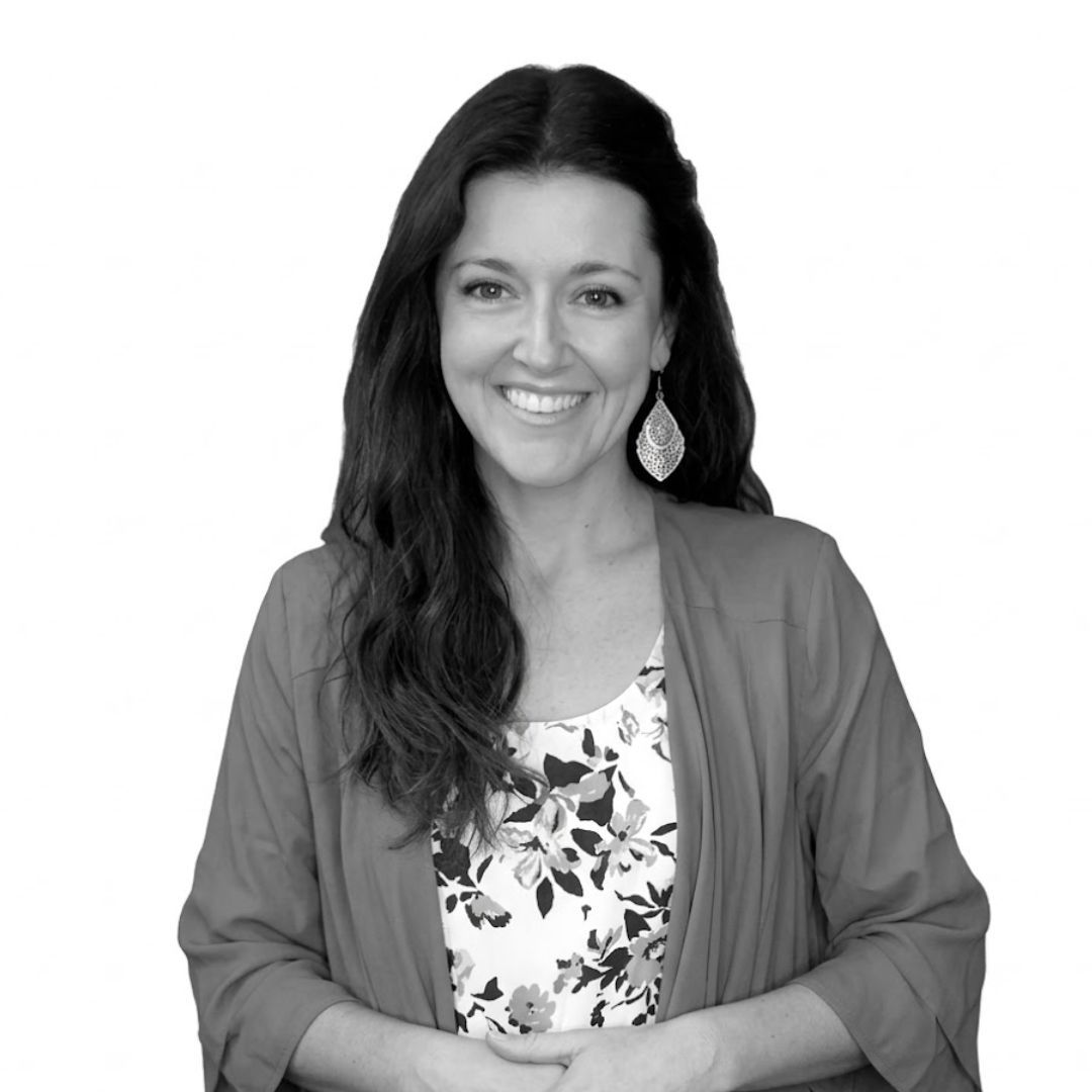 Smiling woman with long dark hair wearing a floral blouse and cardigan, with a dangling earring, facing forward against a plain background