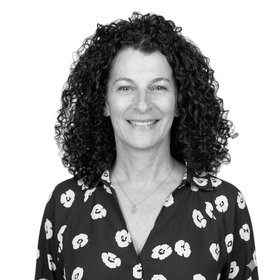 Smiling woman with curly hair wearing a patterned blouse, facing forward against a plain background