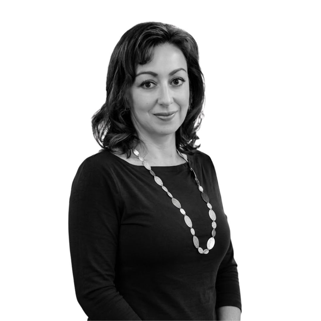 Smiling woman with shoulder-length dark hair wearing a black top and long necklace, facing forward against a plain background
