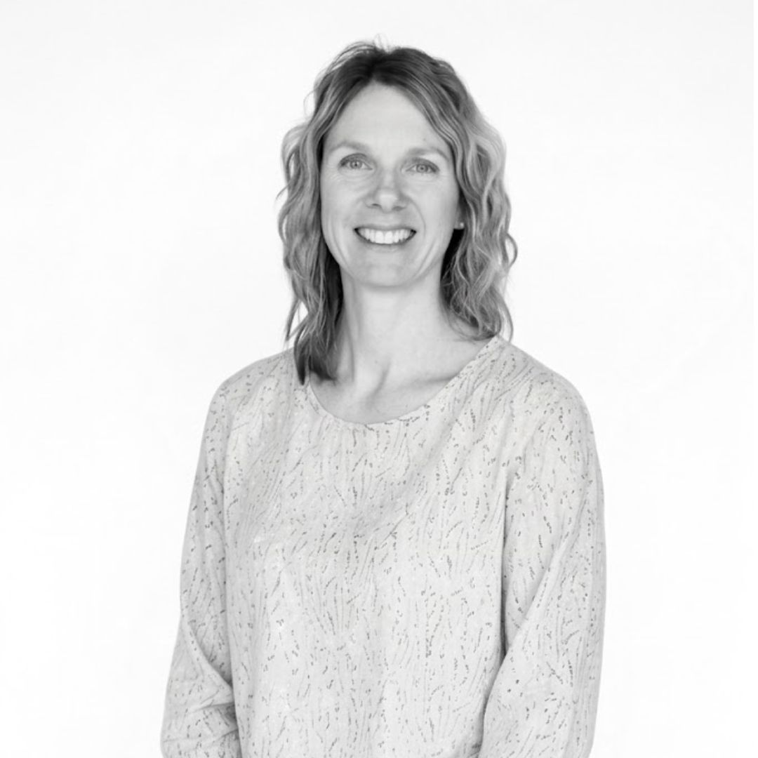 Smiling woman with shoulder-length wavy hair wearing a light textured blouse, facing forward against a plain background