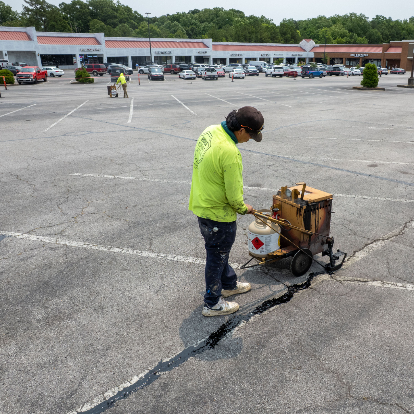 Worker Alabama performing asphalt crack filling in a commercial parking lot to seal cracks and prevent pavement damage