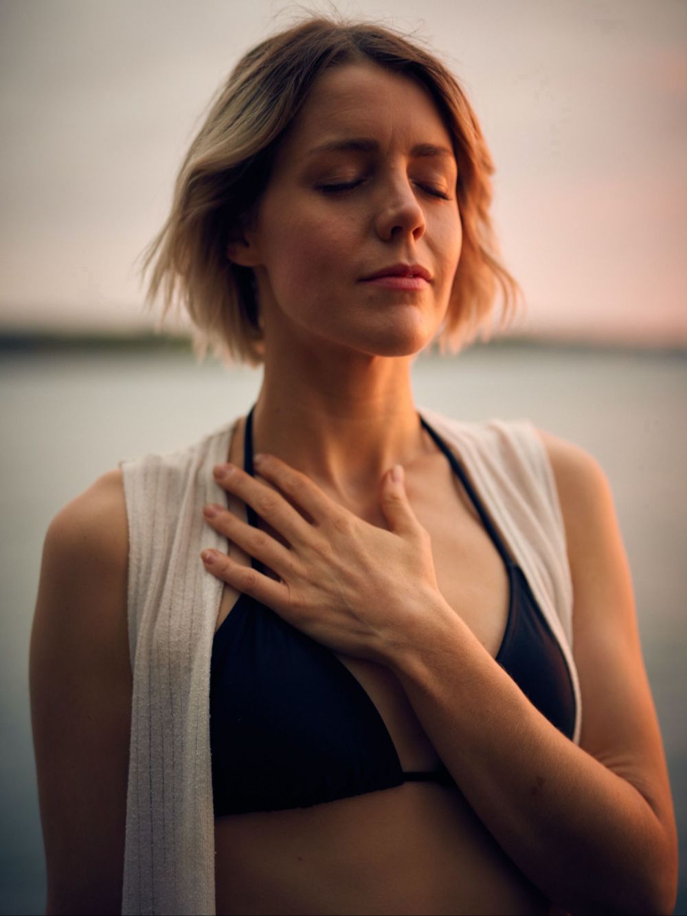 Midlife woman standing peacefully with hand over heart and eyes closed, reflecting inner calm and self-connection.”
