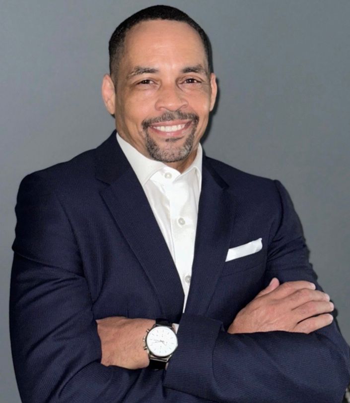 Professional portrait of Steven L. Smith, Certified Self-Transformation Coach, smiling confidently in a navy suit against a gray background.