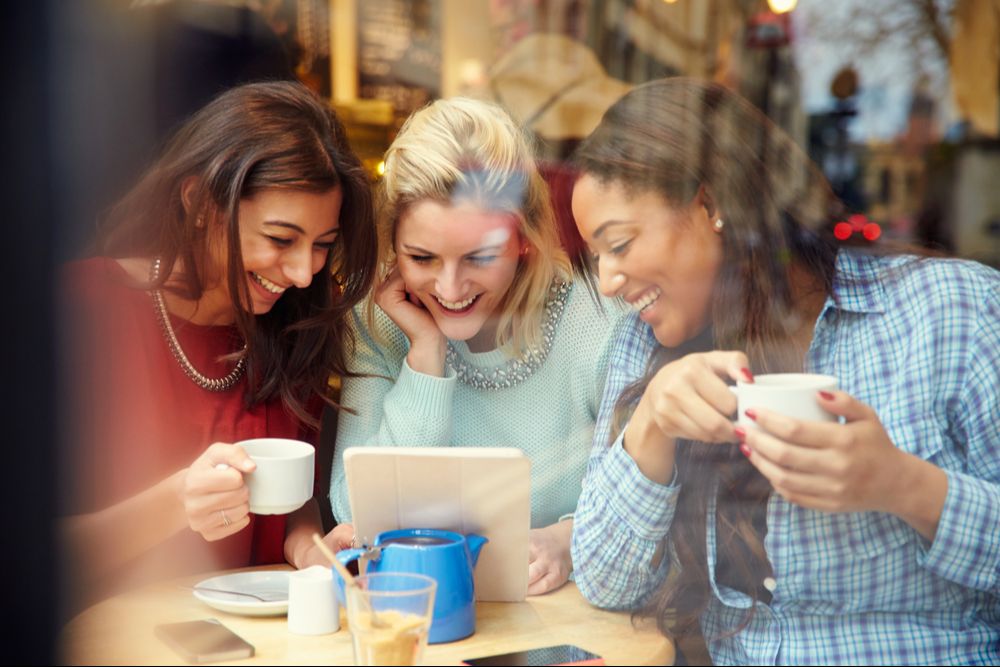 Three women talking together over coffee, looking at a tablet