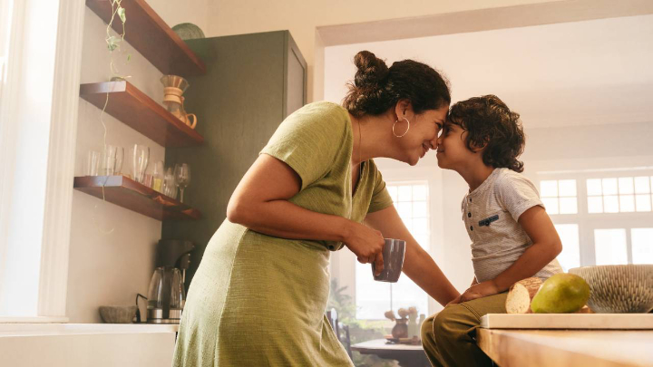 Maman souriante qui touche front contre front avec son enfant dans la cuisine, moment de tendresse et de connexion.