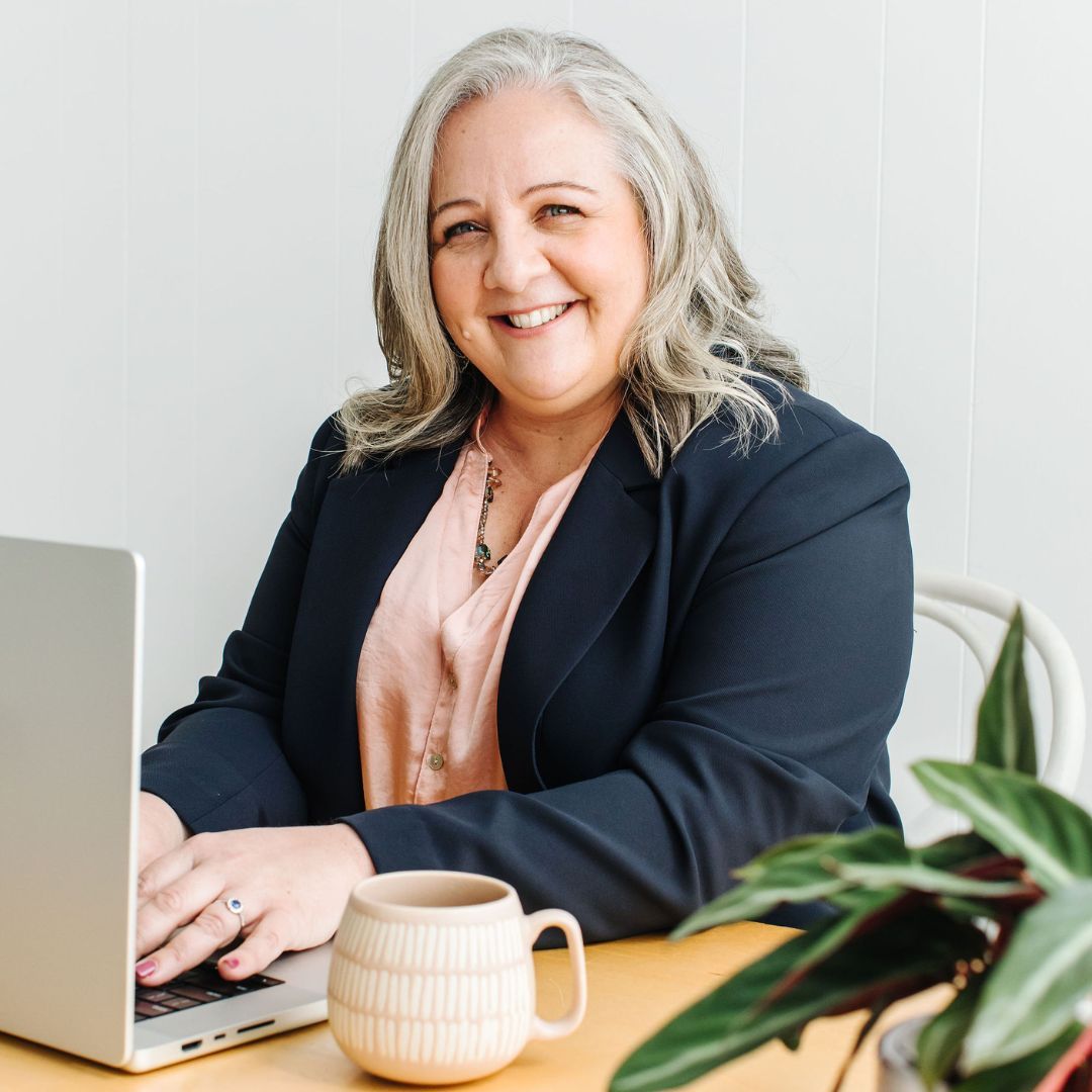 Nicki Kuurman sitting at her desk with a computer, smiling to camera