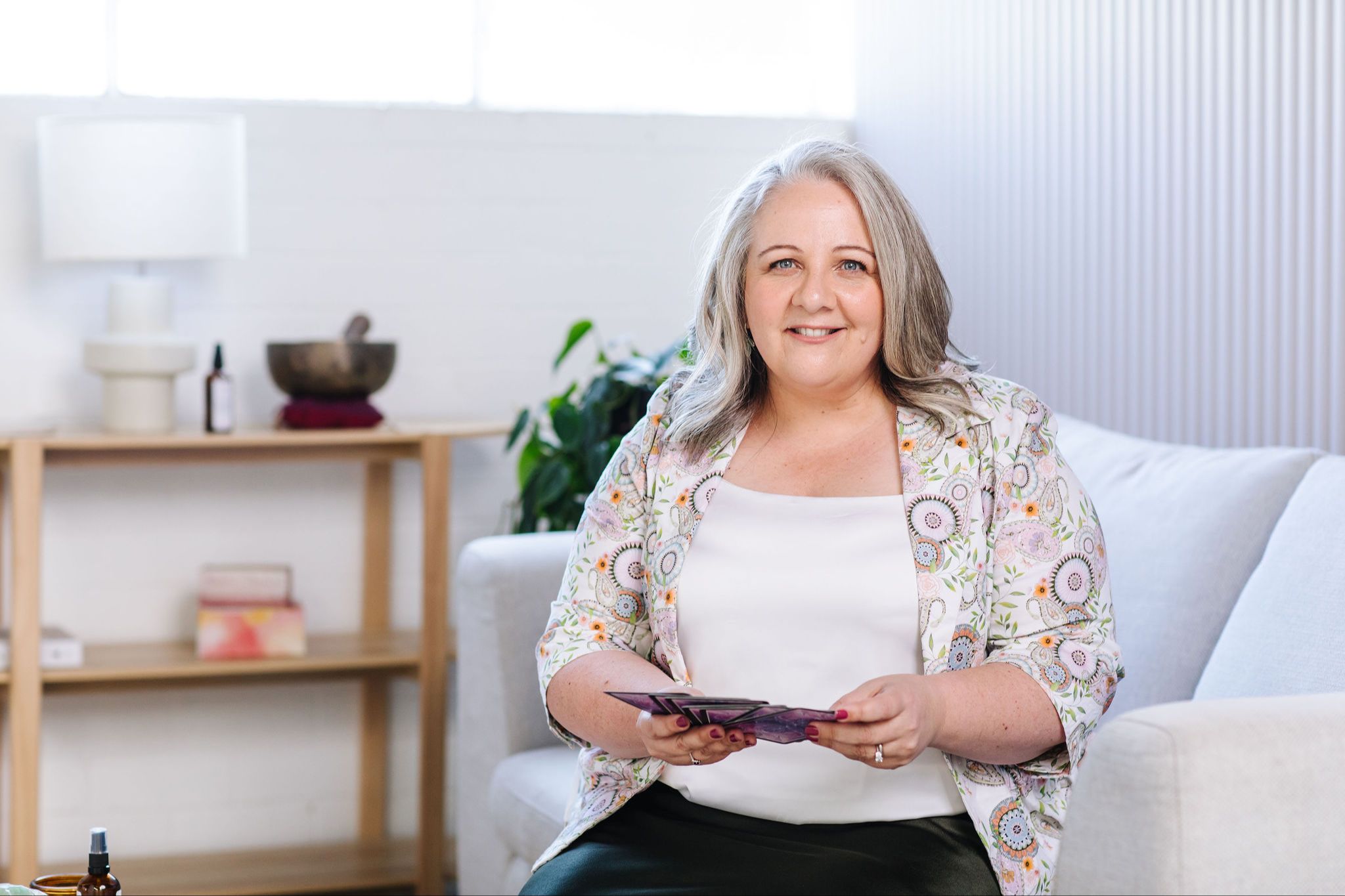 Nicki Kuurman holding oracle cards and sitting on a sofa in her clinic room