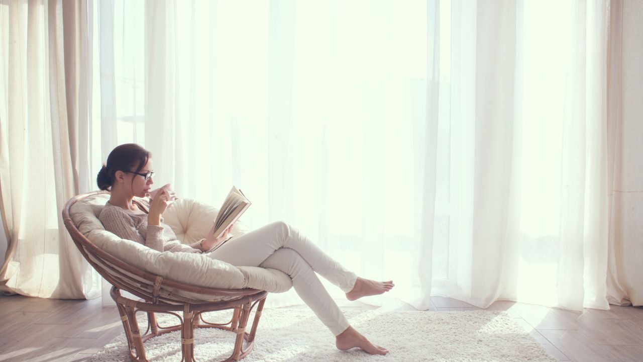 Woman relaxing in a chair with a book, reflecting in a peaceful light-filled space