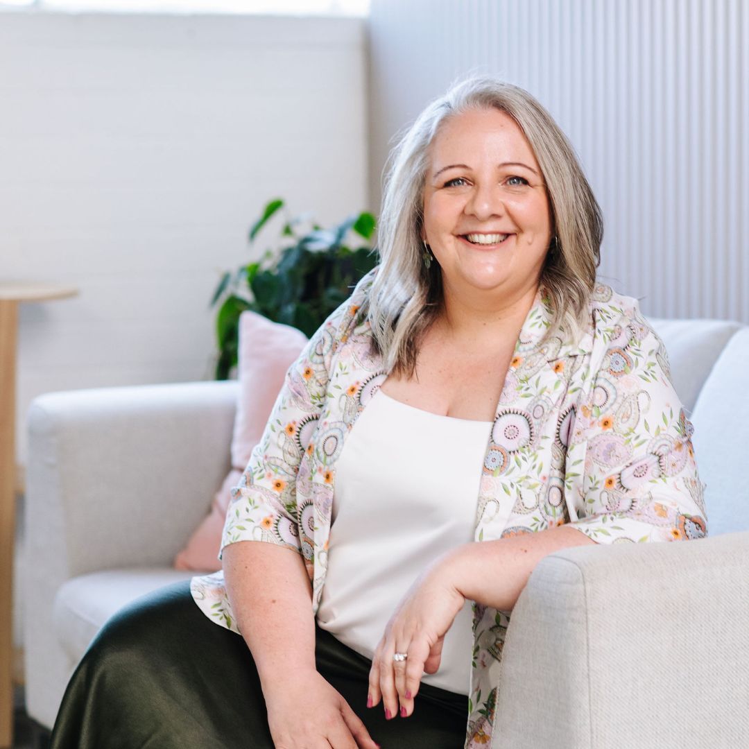 Nicki Kuurman, The Practical Mystic, sitting on a sofa smiling