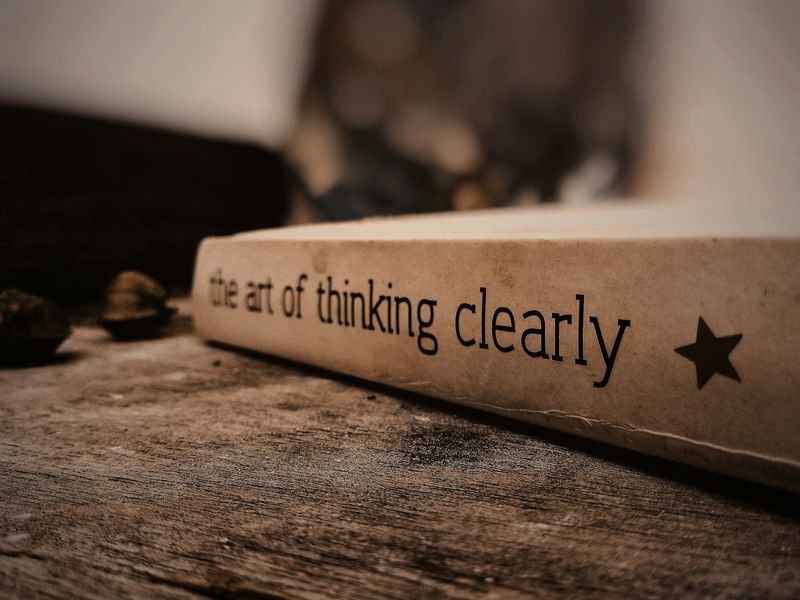 Close-up of a book titled ‘The Art of Thinking Clearly’ on a wooden surface, representing mental clarity, focus, and clear decision-making - Retrained Minds Hypnotherapy.