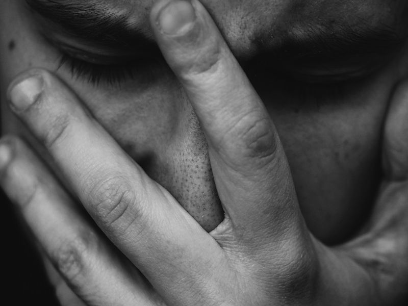 Close-up of a person holding their face in grief, symbolising emotional pain and the process of healing through hypnotherapy.