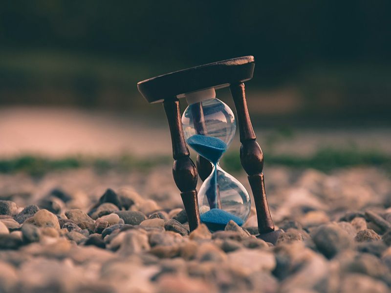 Hourglass standing on pebbles, symbolising time, patience, and the focus needed to achieve motivation and lasting change - Retrained Minds Hypnotherapy.