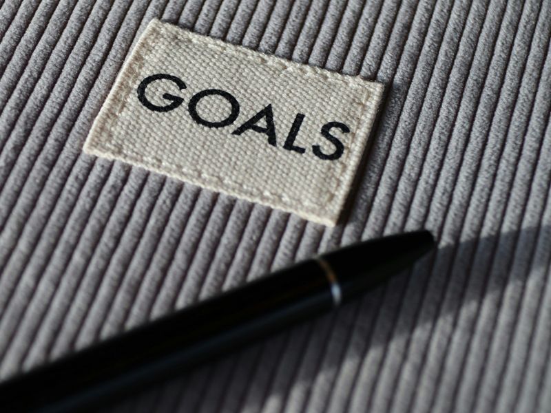 Close-up photo of a pen resting beside a fabric label with the word “GOALS,” symbolising motivation, focus, and goal setting in Retrained Minds hypnotherapy sessions.