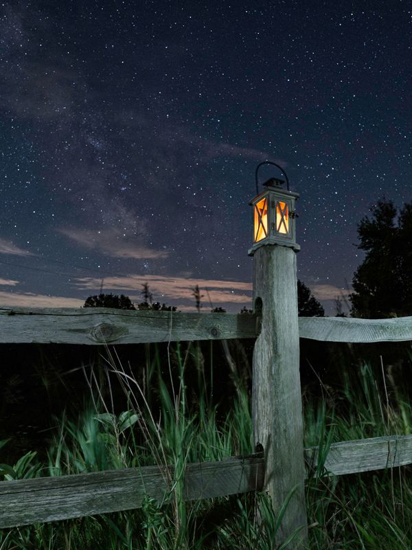 Peaceful night scene with a glowing lantern on a wooden fence under a starry sky, symbolising calm, guidance, and inner peace for anxiety relief.