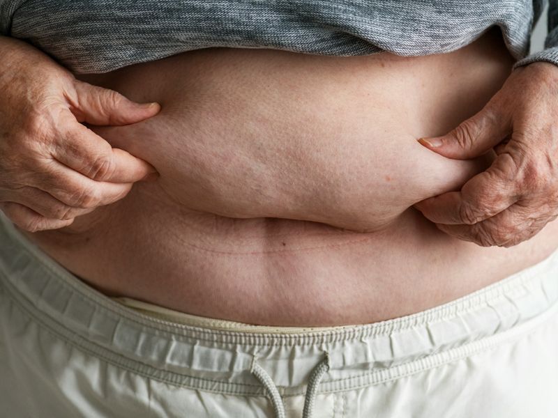 Close-up of a person holding their stomach, symbolising body awareness, acceptance, and the desire for healthy, positive change — Retrained Minds Hypnotherapy.
