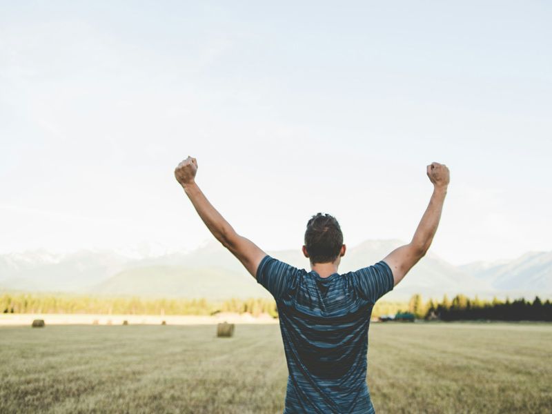 Man standing in an open field with arms raised in triumph, symbolising motivation, confidence, and a positive mindset — Retrained Minds Hypnotherapy.