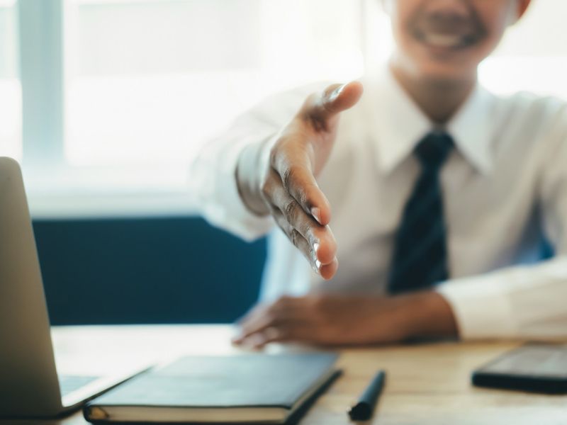A smiling professional extending a hand for a handshake, symbolising confidence, trust, and positive connection in a business meeting.