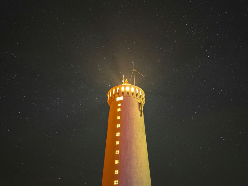 Golden-lit lighthouse shining into a starry night sky, symbolising calm guidance, inner light and clarity for anxiety relief - Retrained Minds Hypnotherapy's "The Lighthouse Within" audio.