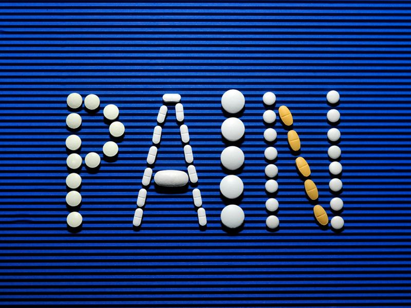 The word ‘PAIN’ spelled out with white and yellow tablets on a blue background, symbolising chronic pain, medication dependence, and the natural alternative relief offered through hypnotherapy - Retrained Minds Hypnotherapy.