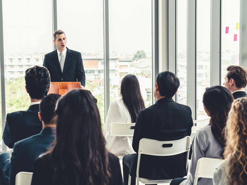A confident speaker delivering a presentation to an attentive audience during a seminar, representing public speaking confidence and performance coaching by Retrained Minds Hypnotherapy.