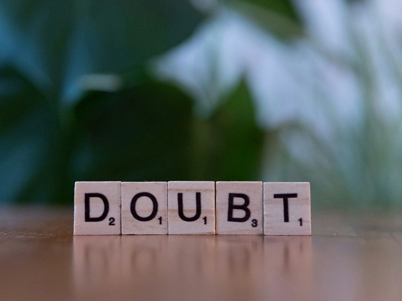 Wooden letter tiles spelling the word “doubt” on a reflective surface, symbolising overcoming self-doubt and rebuilding confidence.