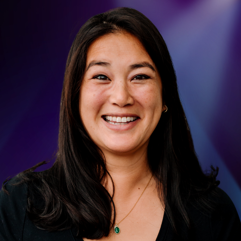 Headshot of an Asian woman with long dark hair and a big smile wearing a black shirt with a delicate necklace