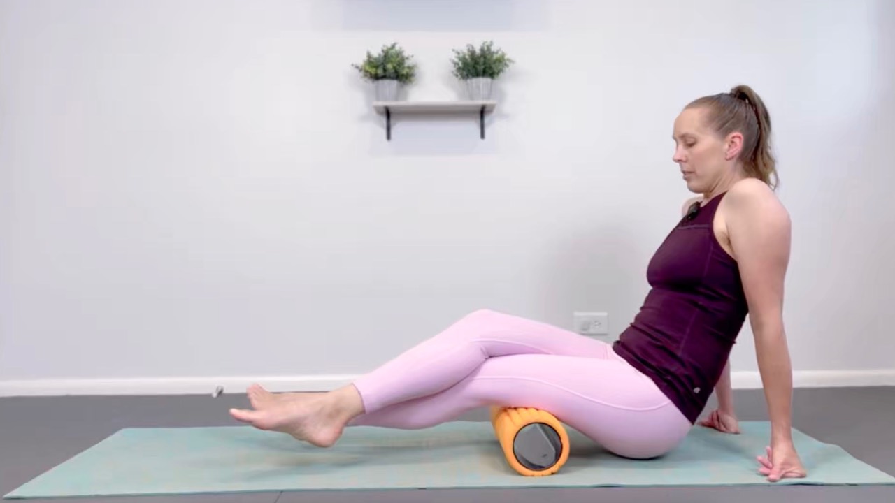 Woman on a yoga mat foam rolling her upper back for The Complete Wellness Bundle.