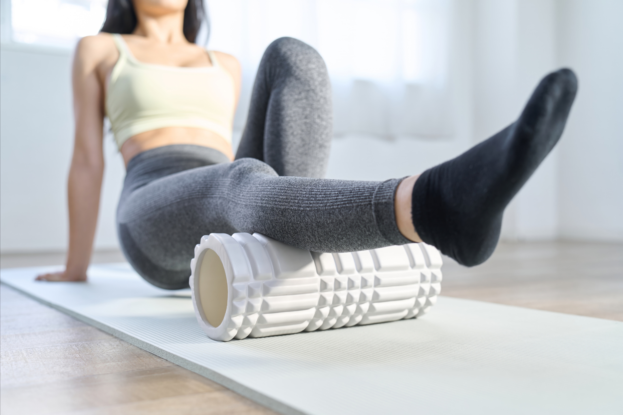 Woman on a yoga mat foam rolling her upper back for The Complete Wellness Bundle.