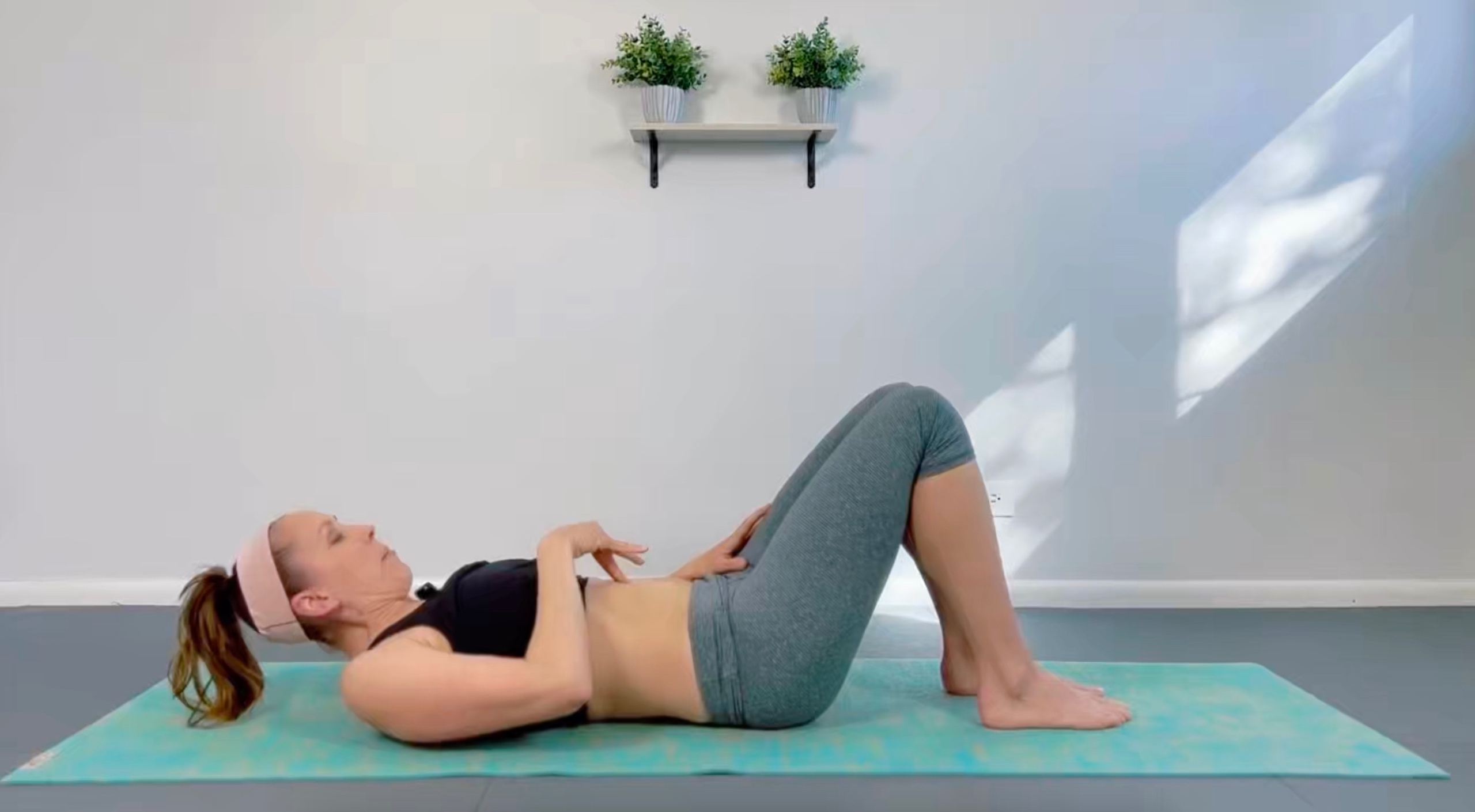 A mom is on a mat with her legs in the air. A baby lays on her legs while mom does a postpartum recovery workout.