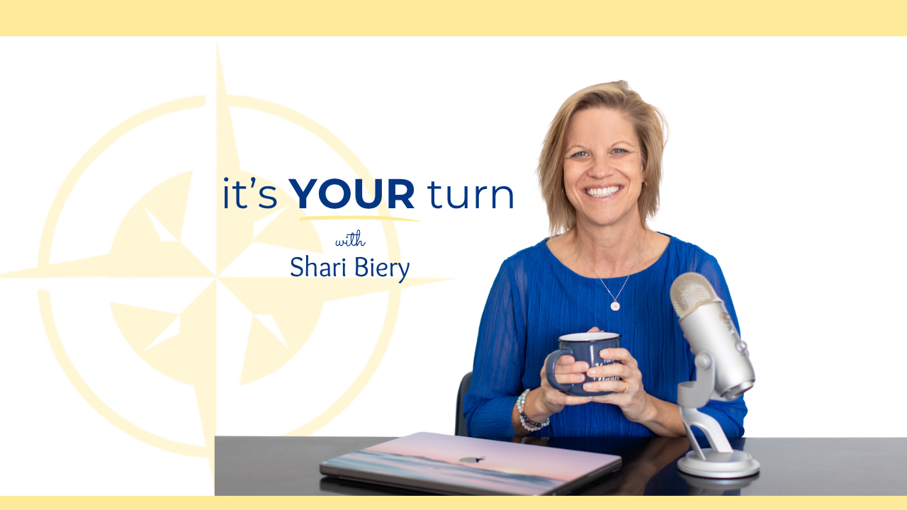Shari smiling with mug over desk and podcast mic