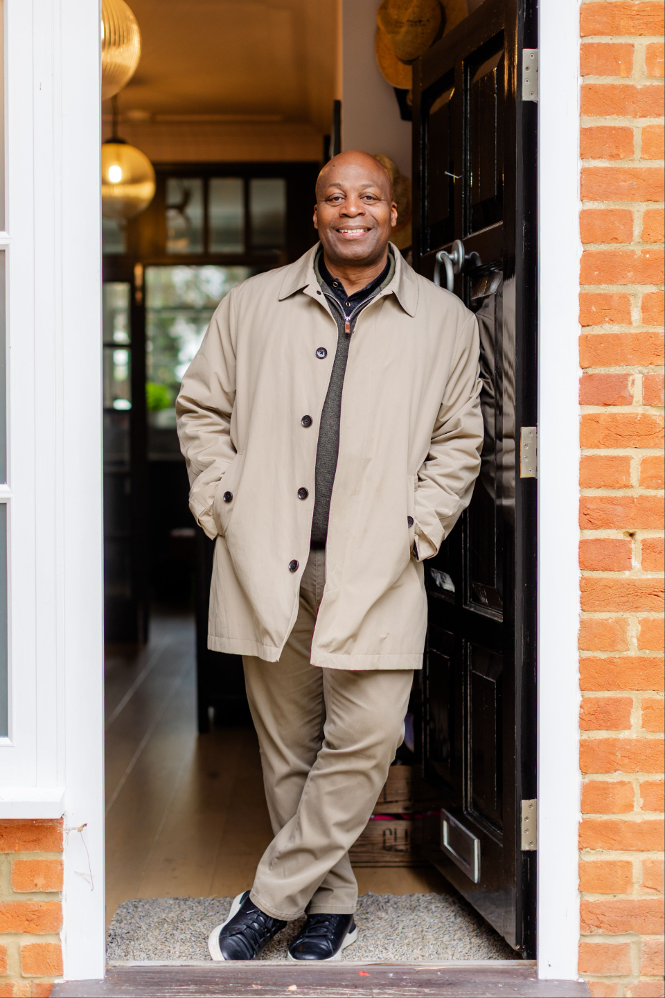 Mike standing in a doorway, smiling and wearing a beige coat.