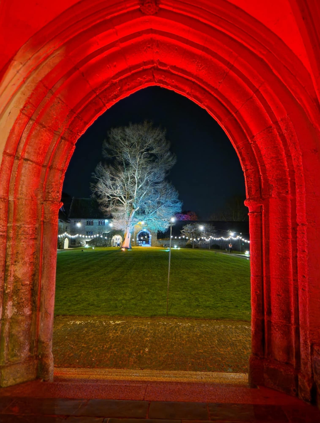 Red-lit Great Hall archway opening onto the courtyard at Dartington Hall.