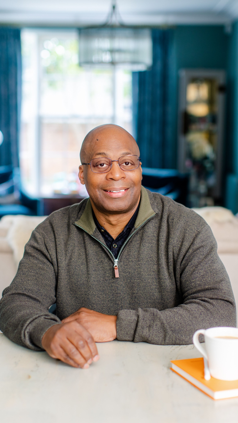 “Mike sitting at a table and smiling, with a notebook and coffee cup in front of him.”