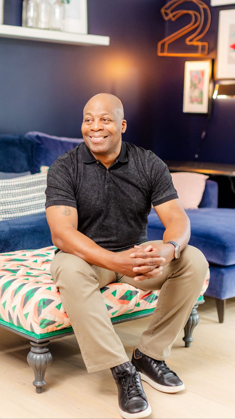 “Mike sitting on a patterned bench and smiling in a modern living room.”