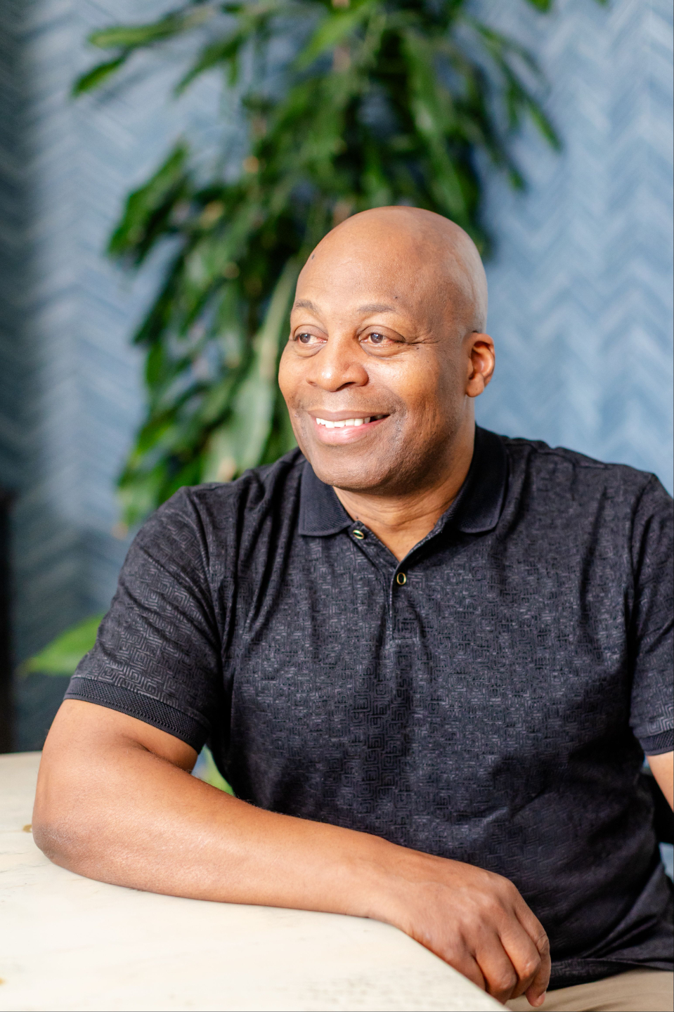 Mike sitting at a table and smiling, with a plant in the background