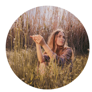 woman sitting in long grass, contemplative look on face