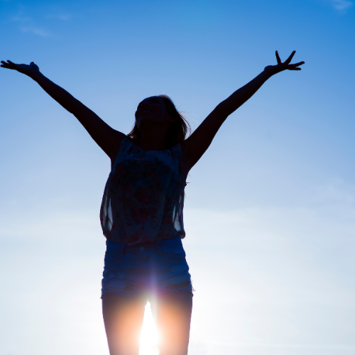Silhouette of a woman in nature, her hands outstretched to the sky