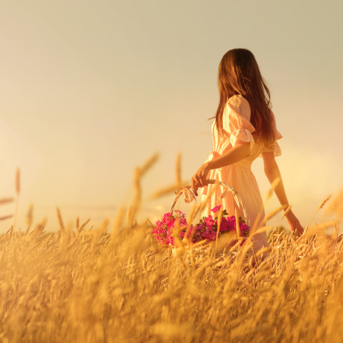 woman walking through long grass holding a basket of flowers