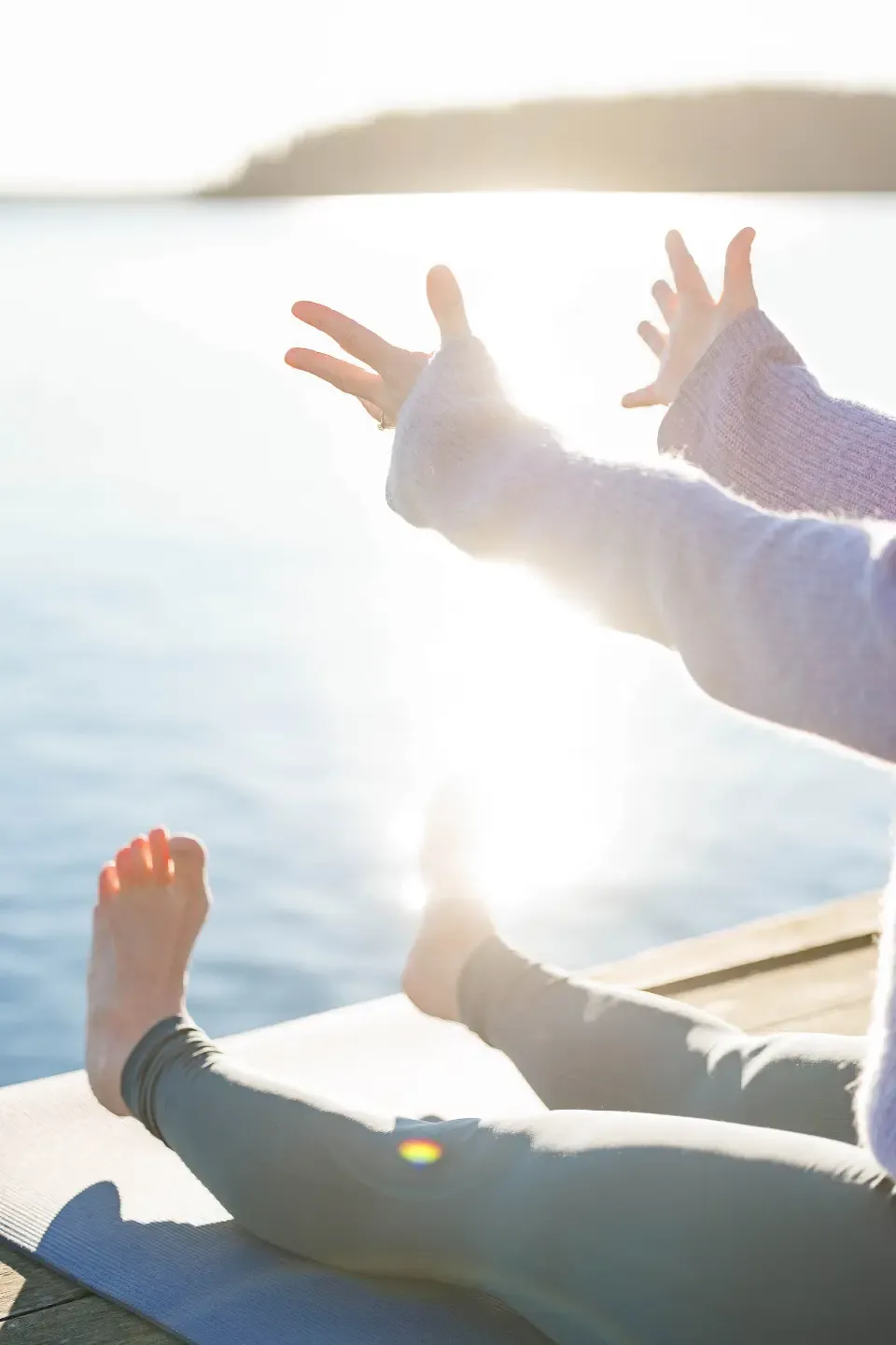 Woman sitting on a yeti in a yoga pose. Stretching her hands and feet in front of her towards the lake. The sun is shining and creating sparkles on the water.