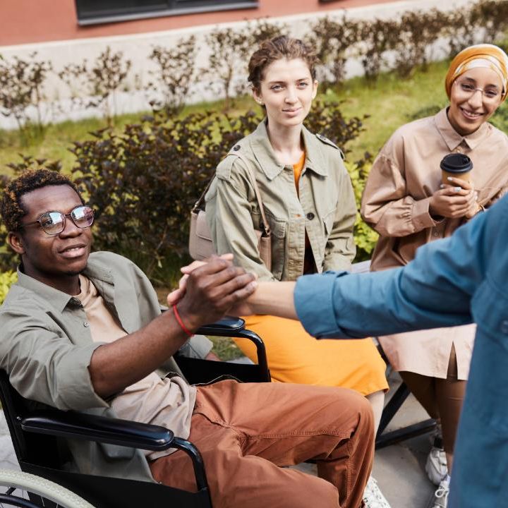 Group of friends having coffee, one is shaking hands with another who is in a wheelchair