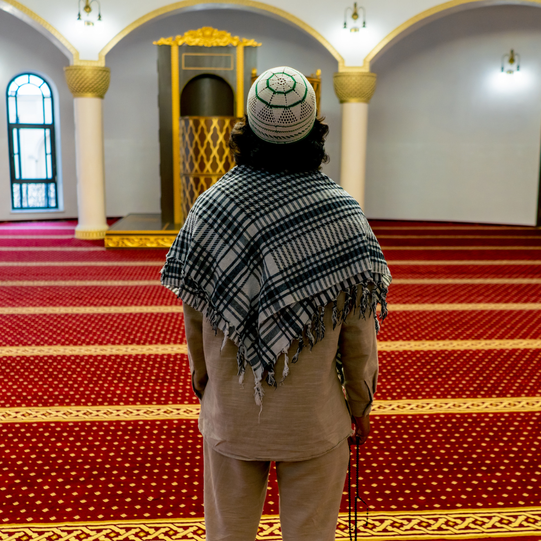 Man dressing in traditional Islamic clothing in a prayer hall looking around.