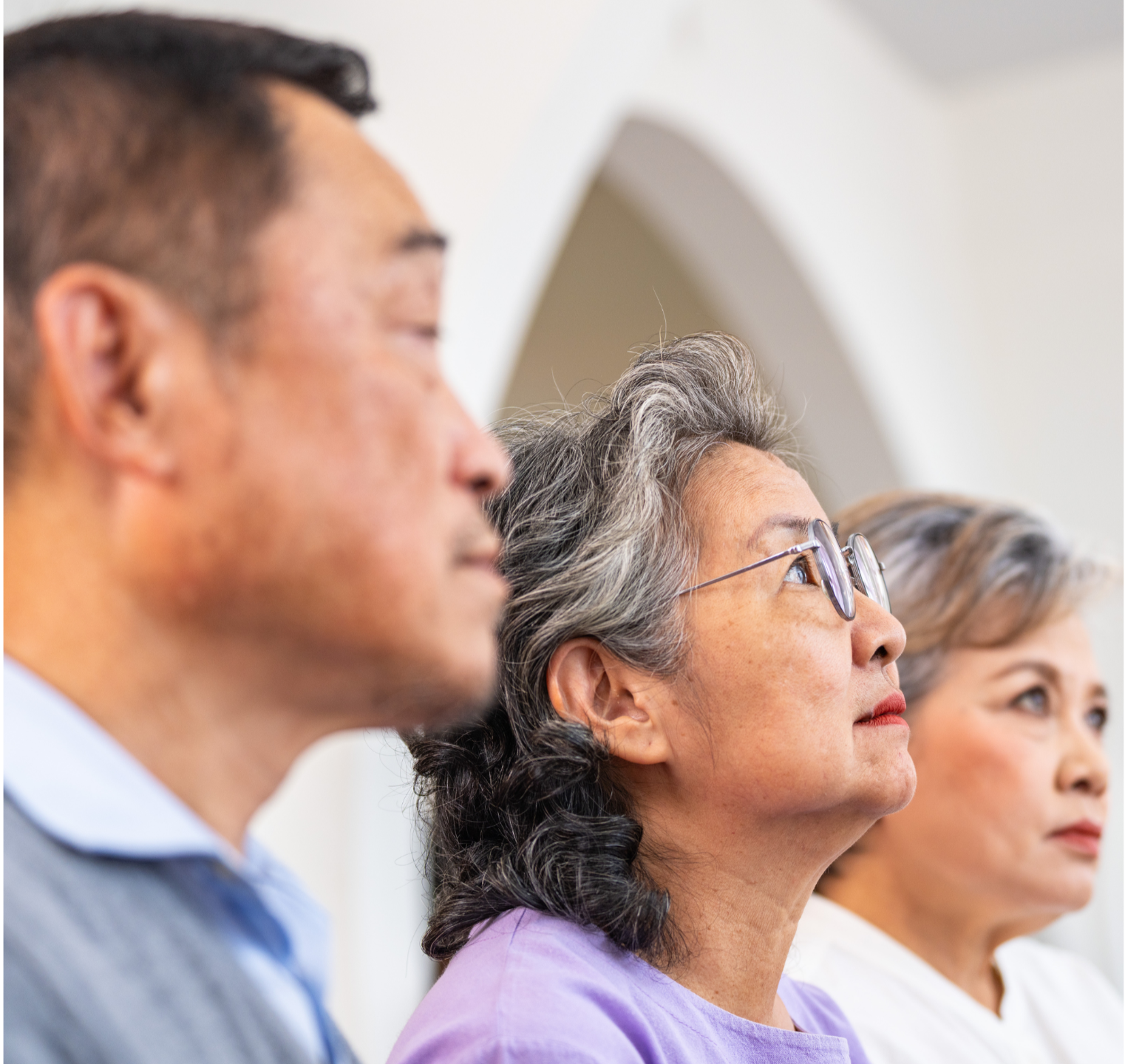 Three older adults looking upwards in a house of worship