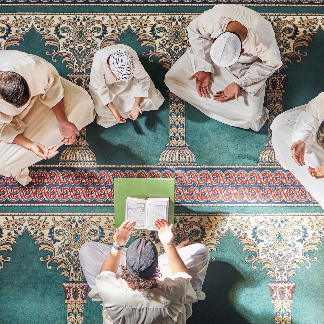 4 men praying in a Mosque, one reading from a book 