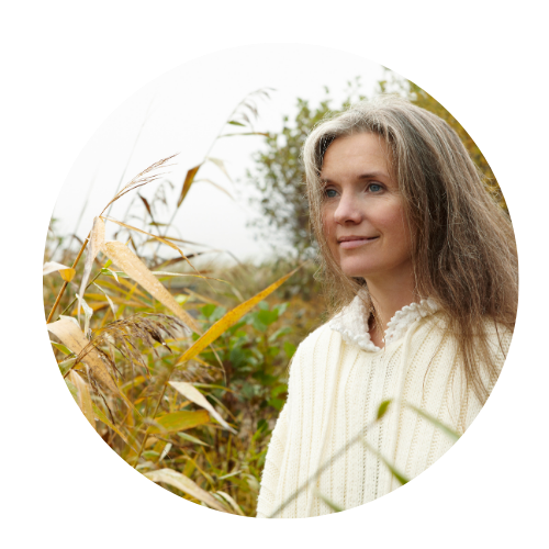 woman smiling looking off to the distance. She is standing amongst tall plants in nature. 