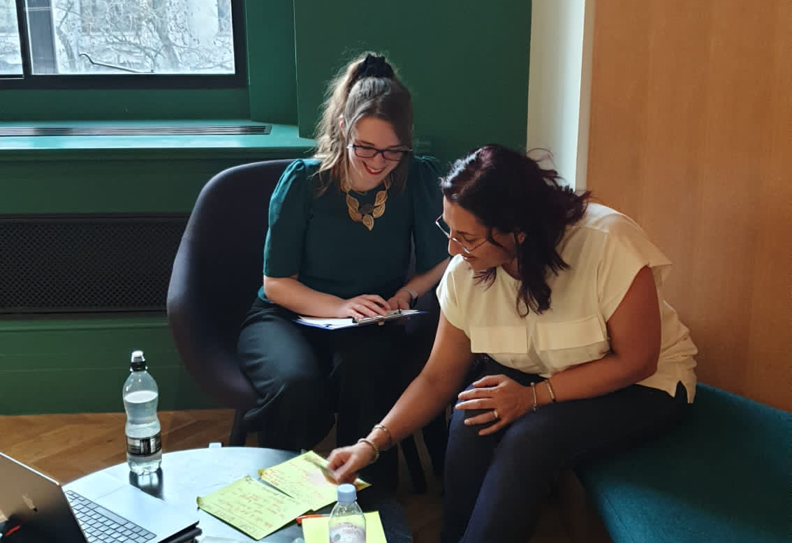 Two female associates sitting at a table together working on post it notes with a laptop