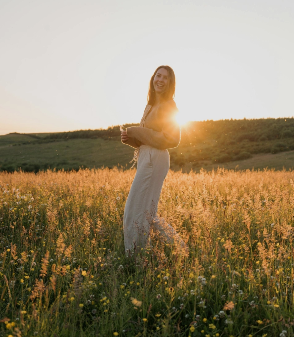 woman in a field of flowers with the glow of the sunset behind her