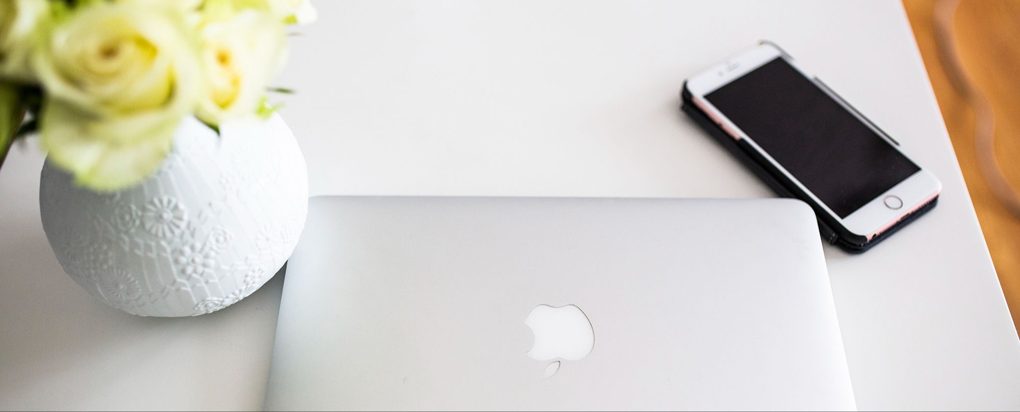 Laptop computer and phone sitting on desk next to a vase of flowers