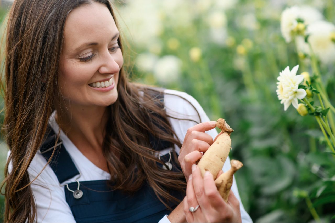 Jennifer smiling and holding up a single dahlia tuber